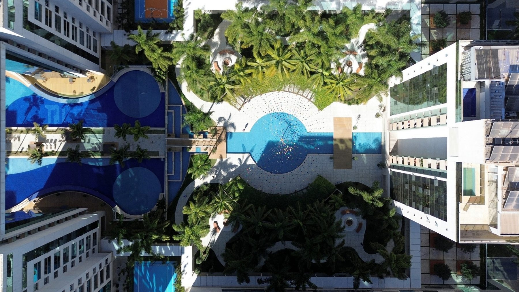 Vista aérea de cima do lazer do condomínio, mostrando piscinas, quadras e jardins