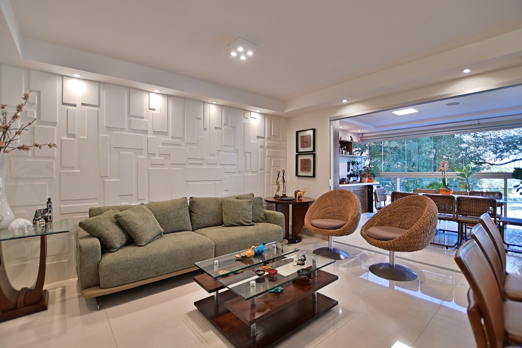 Sala de estar com sofá, poltronas e adega, iluminada por luz natural